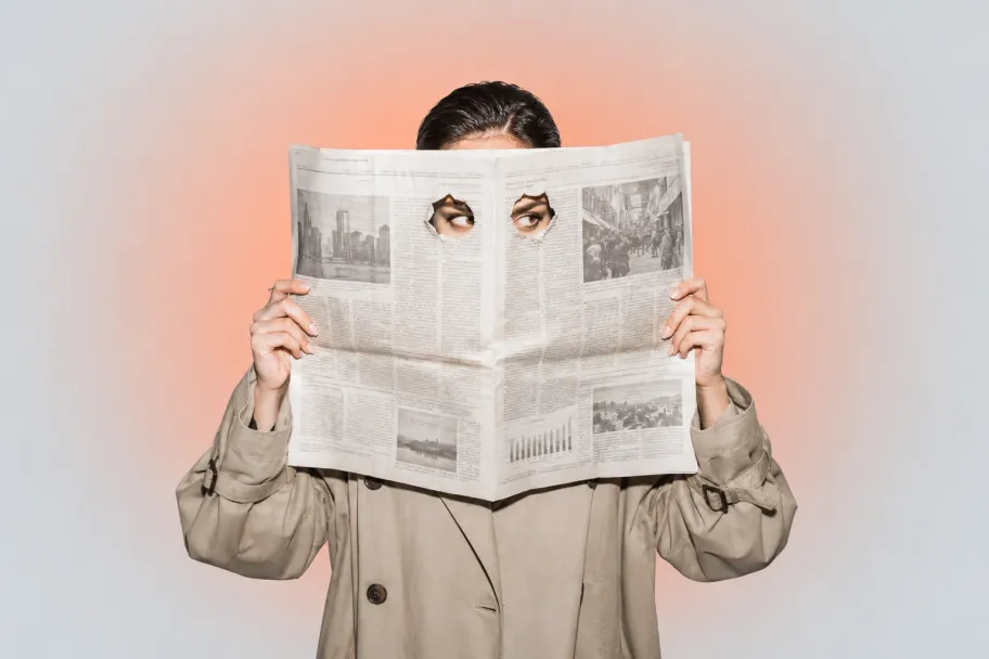 A person in a beige trench coat peering through two eyeholes in a newspaper, on a warm peach gradient.