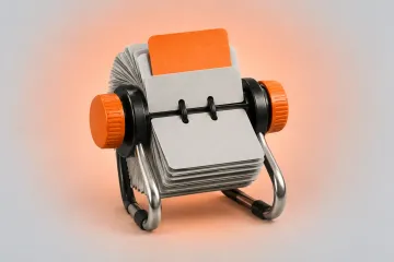 A black and silver rotary card organizer with grey cards, one raised orange card and orange knobs, on a warm peach gradient.